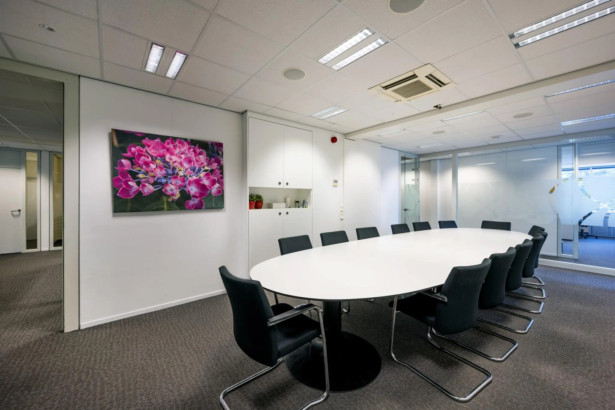 Moderne vergaderruimte aan de Jan Tooropstraat met een ovale tafel, zwarte stoelen en een kleurrijk bloemenschilderij aan de muur.